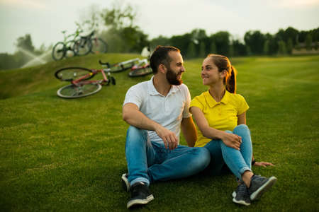 Young beautiful couple sitting on grass in the park. Romantic couple on sunny meadows. Happy summer weekend together outdoors.の写真素材