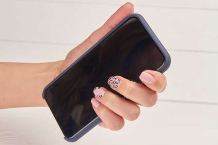 Touch screen phone in female hand. Woman manicured hand holding black cellphone on white wooden background.の写真素材