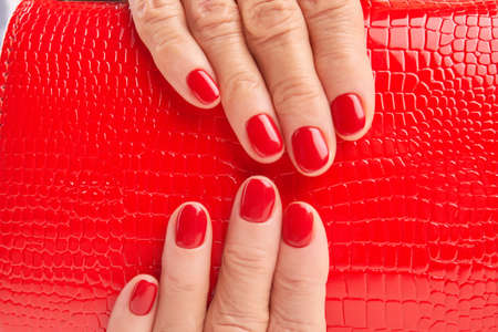 Close up red lacquered handbag in woman hands. Detail of red leather purse in female manicured hands. Beautiful female red manicure.の写真素材