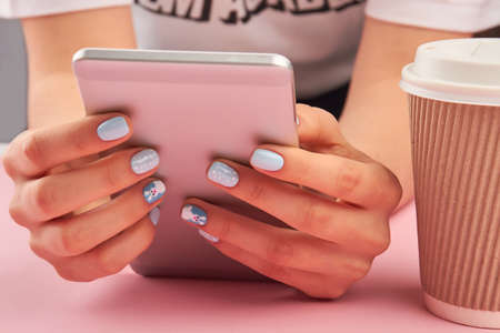 Manicured hands holding pink smartphone. Woman hands with winter manicure using touch screen phone close up. Trendy manicure design.の写真素材