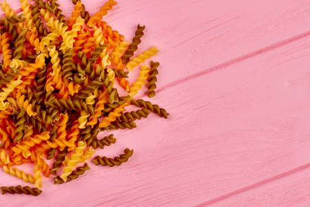 Dried fusilli pasta and copy space. Uncooked spiral macaroni on colorful wooden background and text...