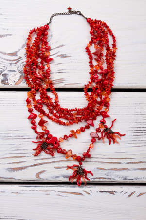 Red polished necklace. Jewelry with little red stones, beige wooden desks surface background.の写真素材