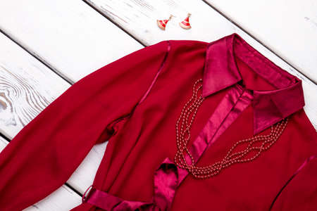 Red silk robe with necklace and earrings. Bright wooden desks surface background.