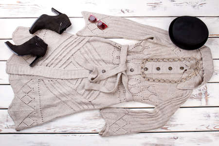 Knitting sweater coat, flat lay. Black suede heel shoes and black berete hat. Bright wooden desk...