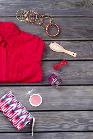 Cosmetic and make-up kit. Red folded womens shirt. Wooden desk surface background.の写真素材