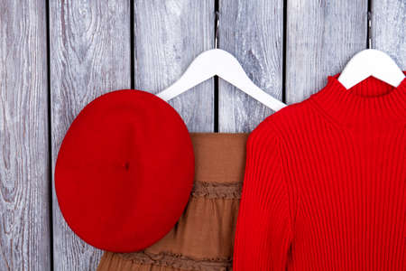 Top view winter outfit on wooden desk. Flat lay, red beret hat, sweater on hangers.の写真素材