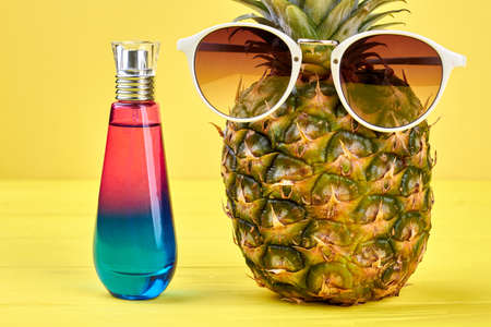 Modern pineapple in sunglasses on color background. Fashion hawaiian pineapple and perfume on yellow background.の写真素材