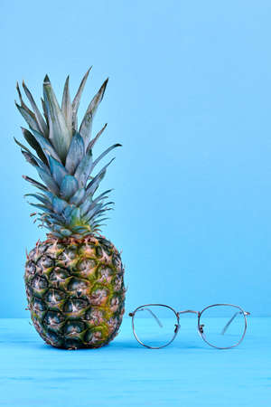 Fresh organic pineapple and eyeglasses. Whole ripe ananas and eyeglasses placed on blue wooden...