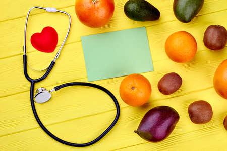 Fresh tropical fruits and stethoscope. Assortment of exotic fruits, heart, blank paper card and medical tool. Fruits diet concept.の写真素材