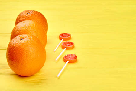 Fresh juicy oranges and sweets on wooden table. Organic oranges fruits and lollipops on yellow...