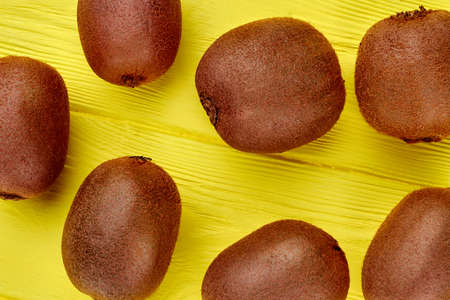 Close up fresh organic kiwi fruits background. Group of ripe brown kiwi fruits on yellow wooden...