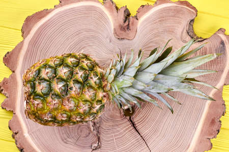 Fresh pineapple on natural wood. Whole organic pineapple fruit placed on tree stump, top view....