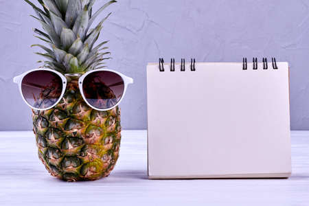 Pineapple in sunglasses and blank notepad. Fresh juicy ananas in sunglasses and empty paper notebook. Vacation plan concept.の写真素材
