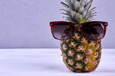 Ananas in sunglasses and copy space. Fresh realistic pineapple fruit wearing sunglasses on wooden background.の写真素材