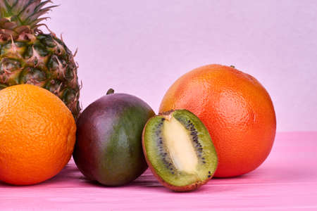 Assorted ripe fruits on color background. Composition from tropical fruits on pink background. Half...