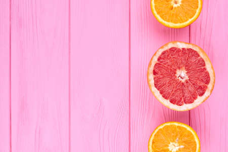 Border fom sliced citrus fruits and copy space. Fresh grapefruit and oranges on pink wooden background with text space.の写真素材