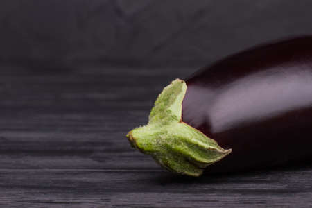 Single dark eggplant on wood. Close up. Black wooden background.の写真素材