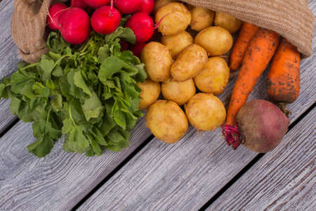 Harvest vegetables in burlap sack on wood. Top view, flat lay.の写真素材