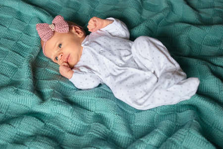 Newborn baby girl with bow in white footed pajamas. Top view. Child on green wool clothes.の写真素材