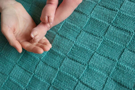 Newborn baby legs and adult hand. Warm wool green blanket.