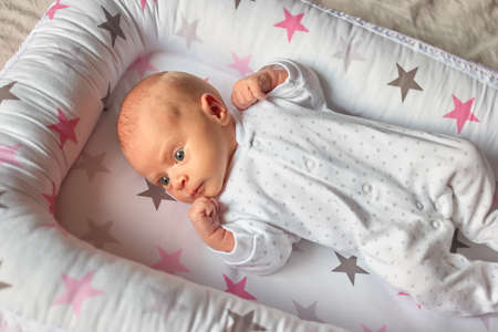 Surprised newborn baby boy in bed. Cute little baby with widely opened eyes.