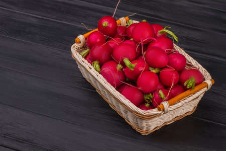 Heap of red ripe radishes in basket. Dark wooden table background.の写真素材