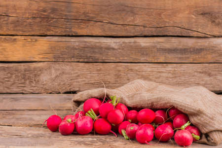 Burlap bag with radishes. Heap of vegetables. Old vintage wooden background.の写真素材
