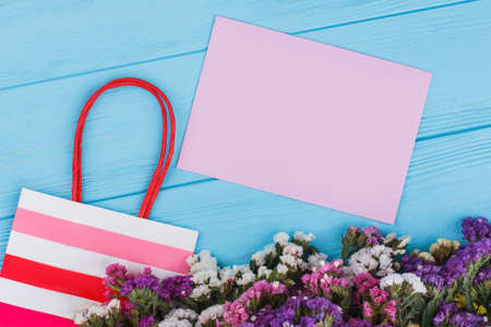 Statice flowers, shopping bag and blank paper for copyspace. Space for text. Blue wooden table...