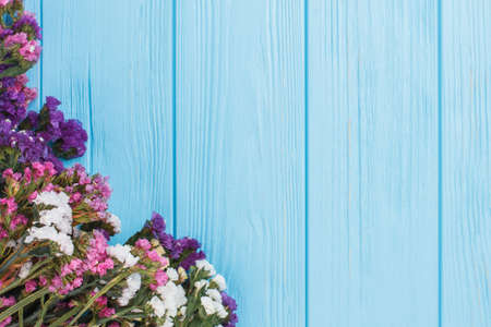 Limonium statice flowers with variety colors. Blue wooden table background. Free space for text.