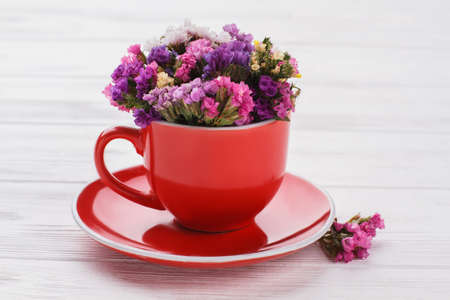 Bouquet of beautiful statice little flowers in a red mug. White wooden table background.の写真素材