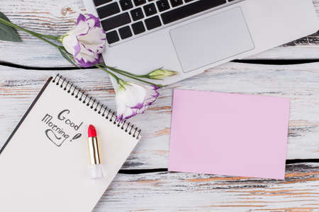 Top view of blank paper, flowers, laptop and lipstick. Flat lay. White wood background.の写真素材