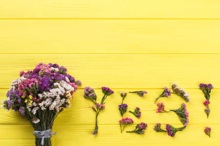 Bouquet of statice flowers and word yes. Top view, copyspace. Yellow wooden table surface background.の写真素材