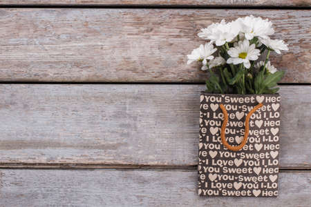 Bouquet of chamomile flowers in shopping package. Old wooden desk surface background. Copyspace, free space for text.の写真素材