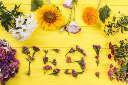 Many different flowers and yes word. Top view. Yellow wooden table surface background.の写真素材