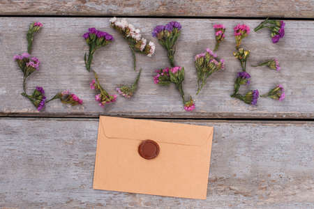Love word made of statice flowers and envelope with wax. Top view. Old vintage wooden desk surface background.の写真素材