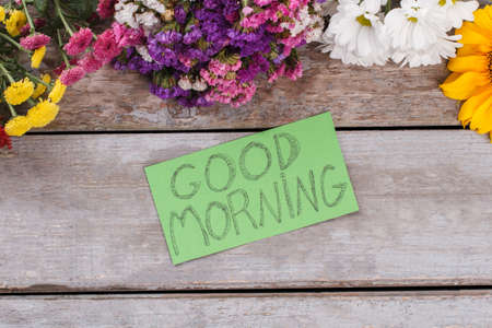 Multicolored statice flowers and good morning wish. Old vintage wooden desk surface background.