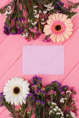 Mail envelope and flowers. Statice lowers. Pink wooden background.
