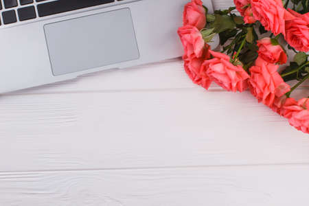 Laptop pc and rose flowers. White wood background.の写真素材