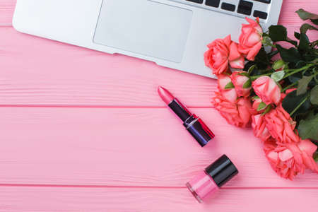 Rose flowers bouquet, lipstic, lacquer and laptop. Flat lay, top view. Pink wooden table surface.の写真素材
