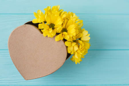 Heart shaped box and yellow jerusalem artichoke flowers. Blue wooden background. Top view.の写真素材