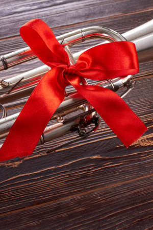 Trumpet with red bow and copy space. Classical musical instrument with red ribbon on wooden background, cropped image.の写真素材