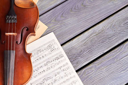 Violin on old wooden boards. Sheets of musical notes and violin on wooden surface with text space....