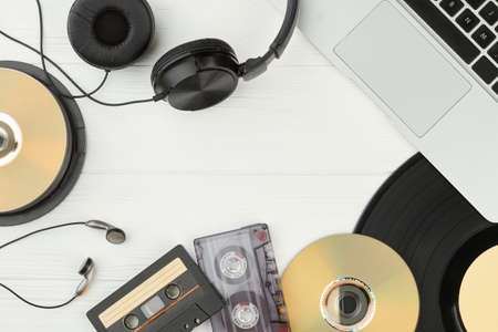 Table with audio music technologies. Frame from laptop, vinyl record, earphones, compact discs and...