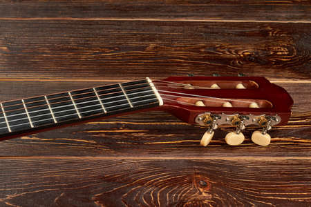Fretboard of guitar on wooden background. Head of acoustic guitar on brown wooden surface. Classical...
