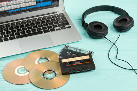 Old and modern equipment on wooden background. Laptop, headphones, audio tape cassettes and compact...