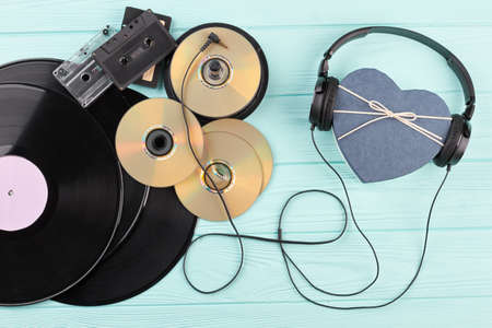 Vinyl records, discs, cassettes and headphones. Headphones with heart-shaped gift box, vinyl records, compact discs and cassettes on wooden background. Musical gift concept.の写真素材