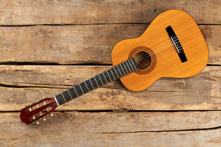 Yellow wooden acoustic guitar. Six strings acoustic guitar on rustic wooden floor, top view.