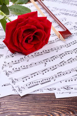 Violin bow and rose on musical notes. Music notes sheets and red rose on wooden background, vertical image. Life is the song.の写真素材