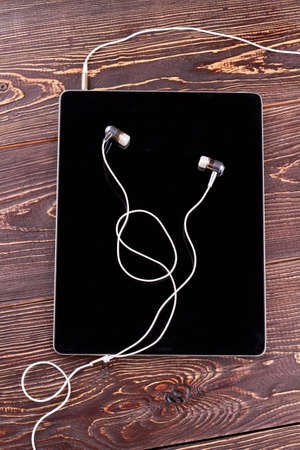 Pc tablet with earphones on wooden background. Digital tablet and headphones on brown wooden...