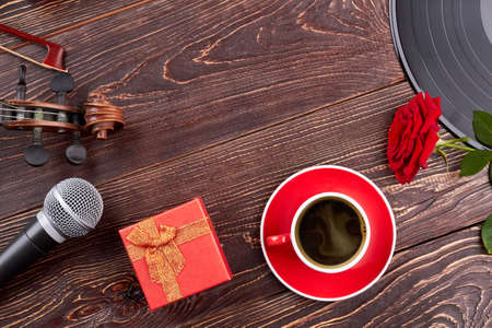 Background with musical equipment, flower and gift box. Violin, microphone, red gift box, cup, rose, vinyl record and copy space. Music still life.の写真素材
